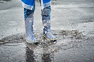 child in blue rubber boots jumping over the puddle in the rain