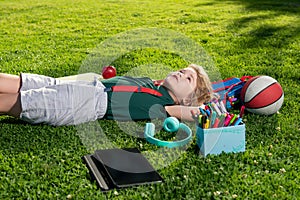 Child with book and taplet and resting on the grass after school. Happy boy relaxing on the grass.