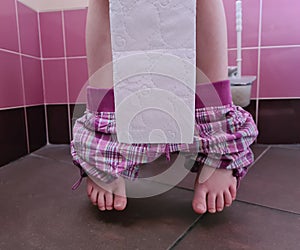 Child with bowel problems and constipation holds toilet paper sitting on toilet