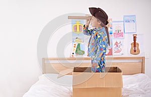 Child, box and pirate hat with spyglasses on bed in home for play, adventure and game as creativity. Boy, cardboard and