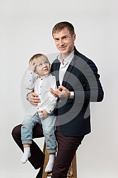 A child boy of 3 years old is sitting in the arms of his father, a young businessman at a photo shoot, a man is looking at the