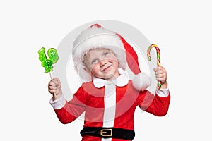 A child boy 4 years old in a New Year costume and a hat of Santa Claus holds colorful bright candies in his hands. Cheerful