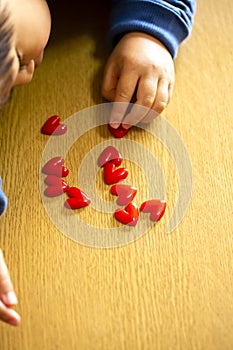 Child boy align the lot red hearts motifs on wooden background