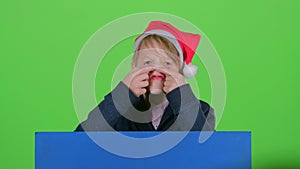 Child boy appeared from behind a blue poster bares his teeth shakes his head and curves of faces and hidden again. Green