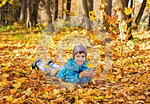 Child boy in autumn park with falling leaves.