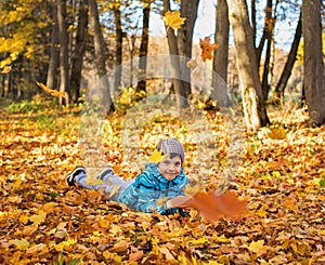 Child boy in autumn park with falling leaves.