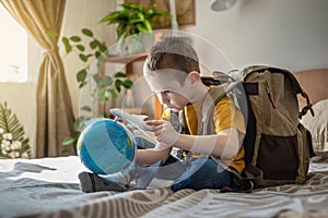 A child boy with backpack is playing with a toy airplane and a globe of the earth. Going on a journey towards adventure