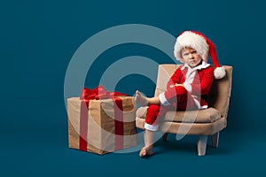 Child boy in bad santa costume with New Year hat, christmas concept. Big gift box with red ribbon. Holiday and congratulations,