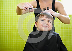 Child, boy and barber with haircut at salon for grooming, hairstyle and unhappy with scissors. Hairdresser, person and