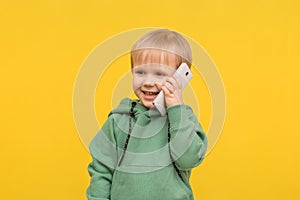 Child boy blond talking on the phone smartphone on a yellow spring background