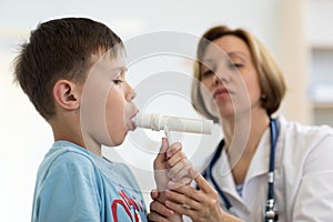 Child boy blowing to peak metr medical device. Doctor examining kid`s lungs