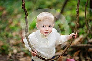 Child boy in a bright sweater with lianas in the forest