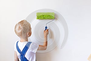 Child boy Builder paints white walls with a roller in an apartment, a child makes house repairs, rear view, place for text
