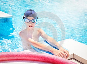 Child (boy) in cap, sport goggles ready to learns professional swimming with pool board, swim noodles.