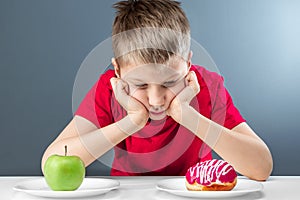 Child boy chooses between a donut and a green apple. Concept Resistance to temptation, fast food, healthy food, diet