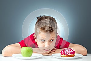Child boy chooses between a donut and a green apple. Concept Resistance to temptation, fast food, healthy food, diet