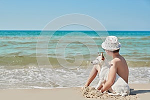 Child boy with dog jack russel on beach. Best friends rest on vacation, play in sand against sea. Tourism and vacation on ocean.