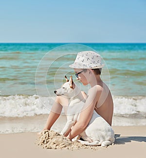 Child boy with dog jack russel on beach. Best friends rest on vacation, play in sand against sea. Tourism and vacation on ocean.