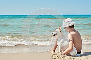 Child boy with dog jack russel on beach. Best friends rest on vacation, play in sand against sea. Tourism and vacation on ocean.