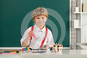 Child boy drawing with coloring pens, painting with early development paints. Portrait school kid boy doing art homework