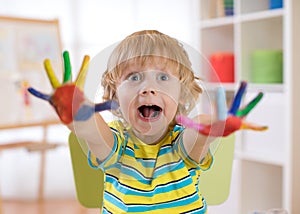 Child boy draws with hands and shows multi-colored painted palms. Children`s educational games with paints.