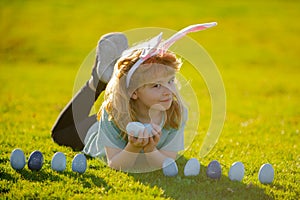 Child boy with easter eggs and bunny ears on grass. Cute kid having fun in park. Easter egg hunt concept. Child boy