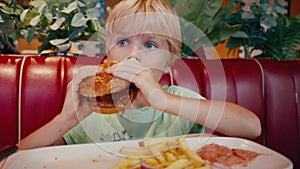 Child boy eating big tasty hamburger in restaurant on lunch or dinner