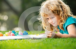 Child boy enjoying art and craft drawing in backyard or spring park. Children drawing draw with pencils outdoor