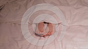 child boy feet under blanket on the sheet at evening. Sleeping baby kid girl with bare legs foot wiggles in her sleep on