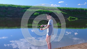 Child boy is fishing in river using spinning rod at summer sunny day on nature.