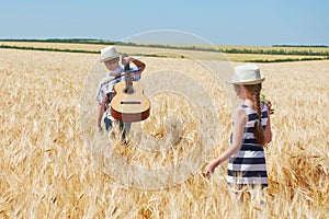 Child boy and girl with guitar are in the yellow wheat field, bright sun, summer landscape