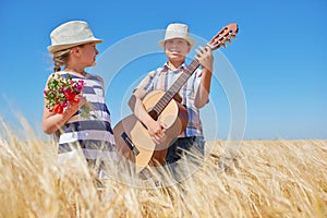 Child boy and girl with guitar are in the yellow wheat field, bright sun, summer landscape