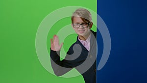 Child boy in glasses peeps out from the blue wall on a green screen