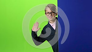 Child boy in glasses peeps out from the blue wall on a green screen. Slow motion