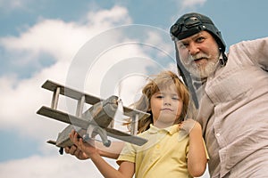 Child boy and grandfather playing with wooden plane against summer sky background. Child boy with dreams of flying or
