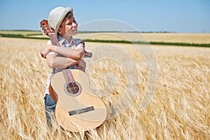 Child boy with guitar is in the yellow wheat field, bright sun, summer landscape