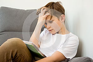 Child boy hardly working on his homework, studying online at home with books and laptop