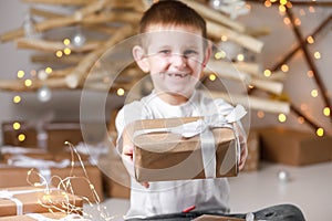 Child boy holding gift box on christmas background. simple gift in kraft paper packaging tied with a white ribbon in the hands of