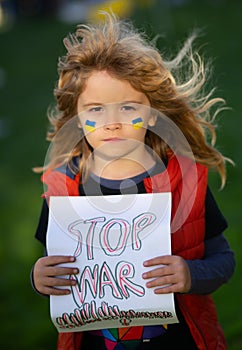 Child boy holding sign with words Stop war standing outdoors. Child carries a sign Stop war. Putin attack Ukrainian