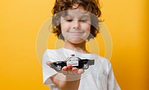 Child boy is holding a toy police car in white tshirt in yellow background. Closeup