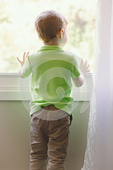 Child boy at home looking out of window outside
