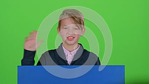 Child boy in jumper emerges from behind the board and waving on a green screen