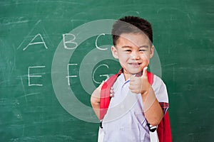 Child boy kindergarten in student uniform with school bag and books smile show finger thumb up
