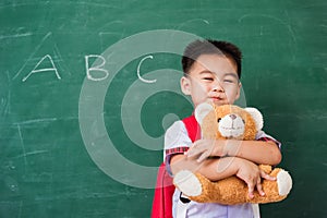 Child boy from kindergarten in student uniform with school bag smiling and hugging teddy bear