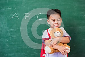 Child boy from kindergarten in student uniform with school bag smiling and hugging teddy bear