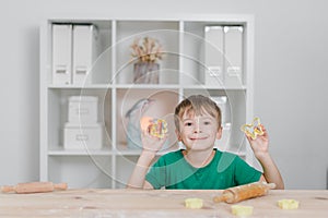 A child boy at the kitchen table demonstrates forms for cooking cookies, he smiles and is happy.