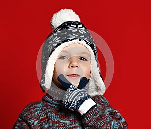 Child boy in knitted hat and sweater and mittens having fun over colorful red background.