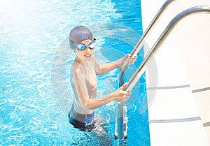 Child (boy) is on ladder handrails (stairs) in to the swimming pool smiling after swimming.