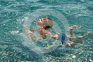 Child boy learning to swim in clear transparent sea.
