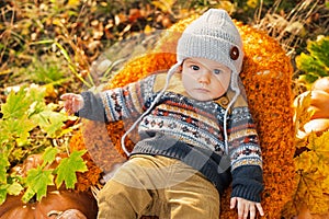 Child boy lies in a basket with pumpkins in autumn leaves.